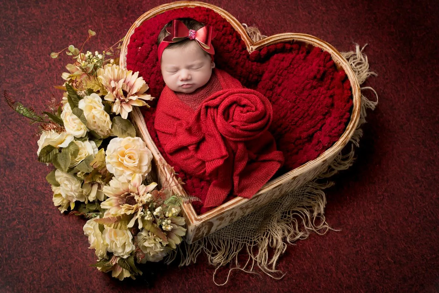 Recém-nascido em uma cesta de coração, com tecido vermelho e flores
