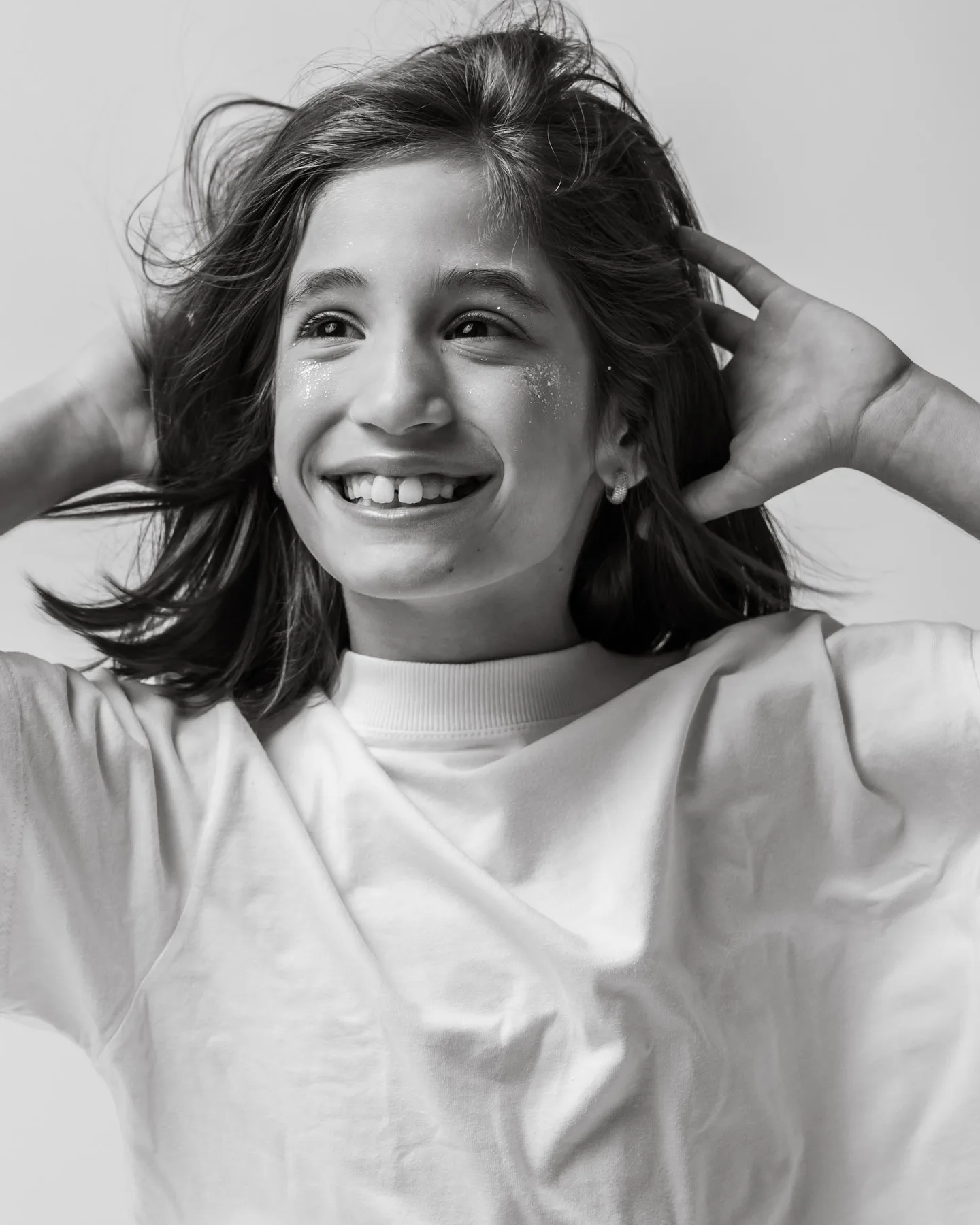 Retrato em preto e branco de uma criança sorrindo com as mãos próximas ao cabelo