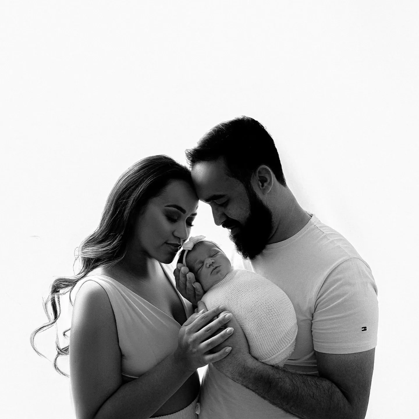 Casal em retrato preto e branco, com as mãos sobre a barriga da gestante