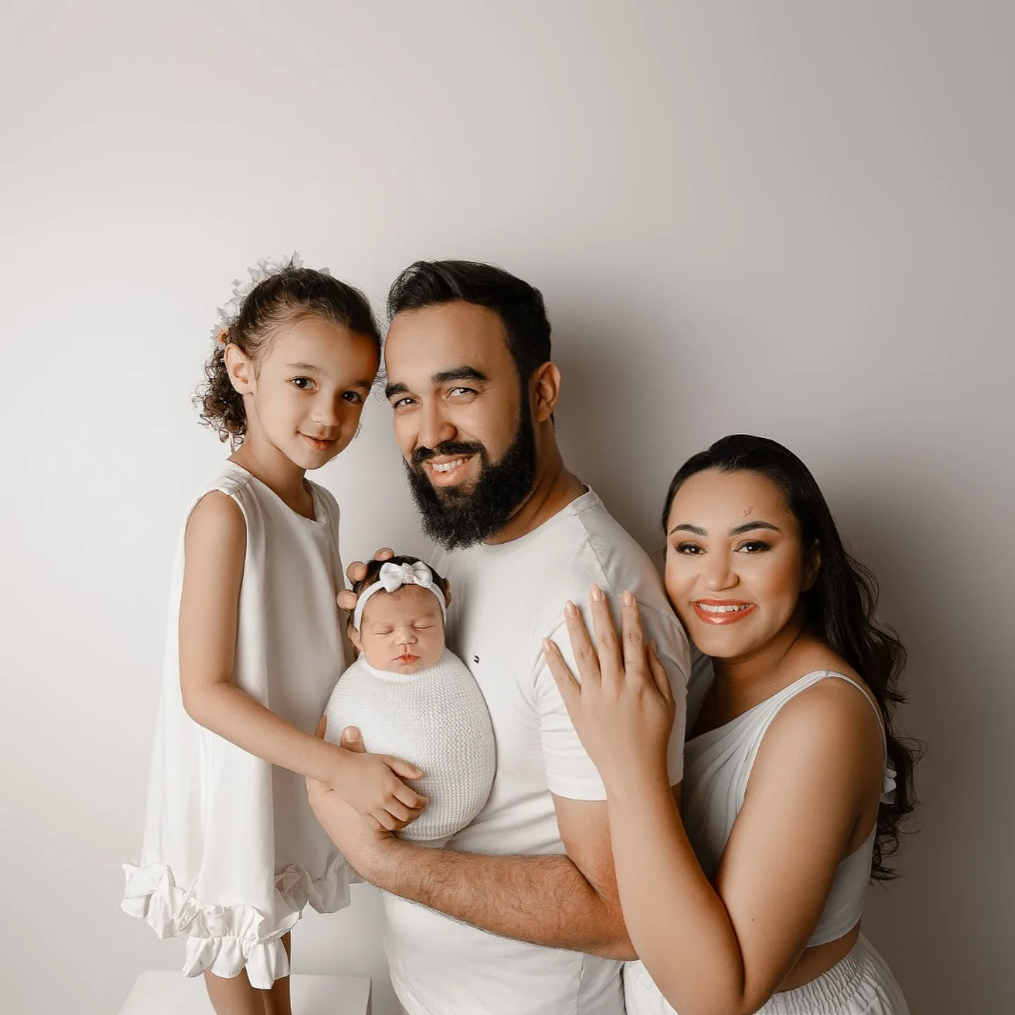 Família reunida com um bebê ao centro em um retrato de fundo claro